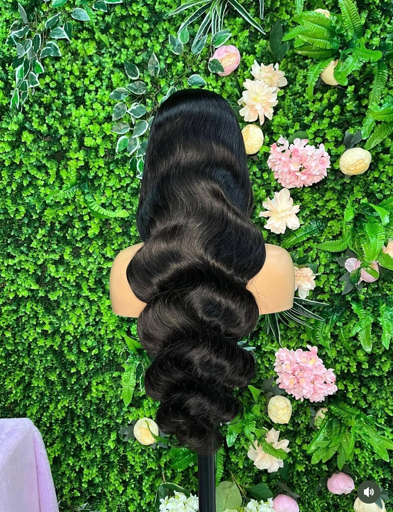 Black hair on a mannequin head against a green foliage and floral background